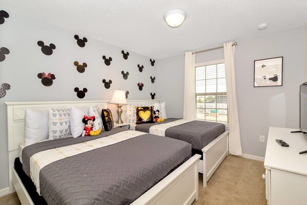 A bedroom with two beds, a nightstand, a lamp, a Mickey Mouse wall decal, and a window with curtains. - Solterra Resort - Lovely 5bd/4ba Pool Home #5st429 (Davenport)