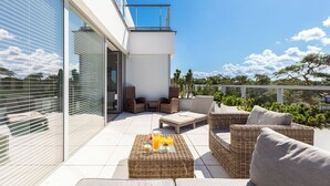 Une terrasse extérieure moderne, avec des meubles en osier, une porte vitrée donnant sur l’intérieur et une vue sur le paysage environnant.