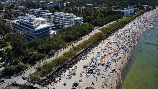 Un paysage urbain côtier avec des bâtiments modernes, une plage animée et un ciel dégagé.