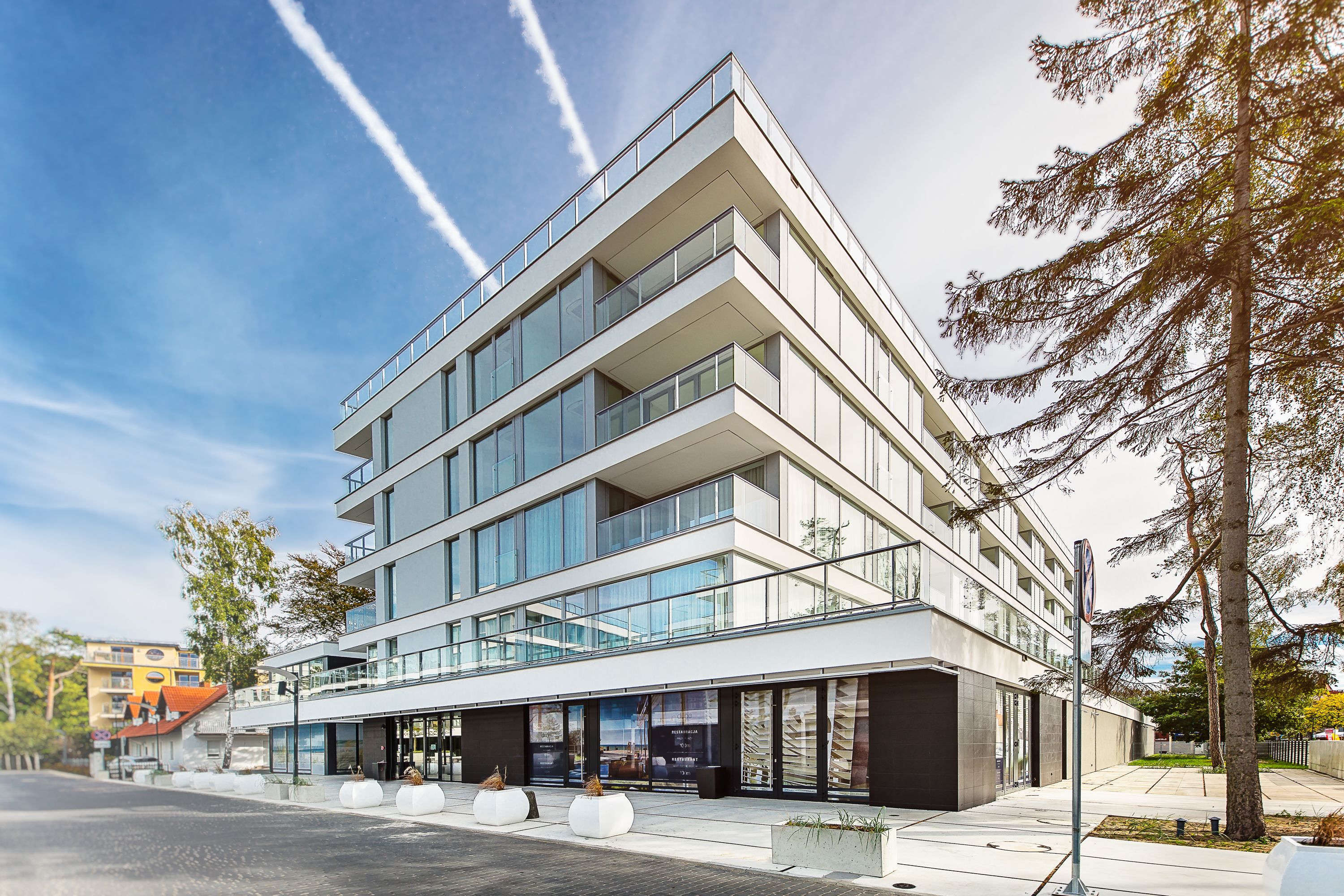 A modern multi-story building with large windows and balconies, situated on a sunny day.
