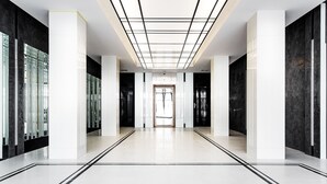 Un couloir d’hôtel moderne avec un sol carrelé, des murs blancs et un plafond à motifs géométriques.