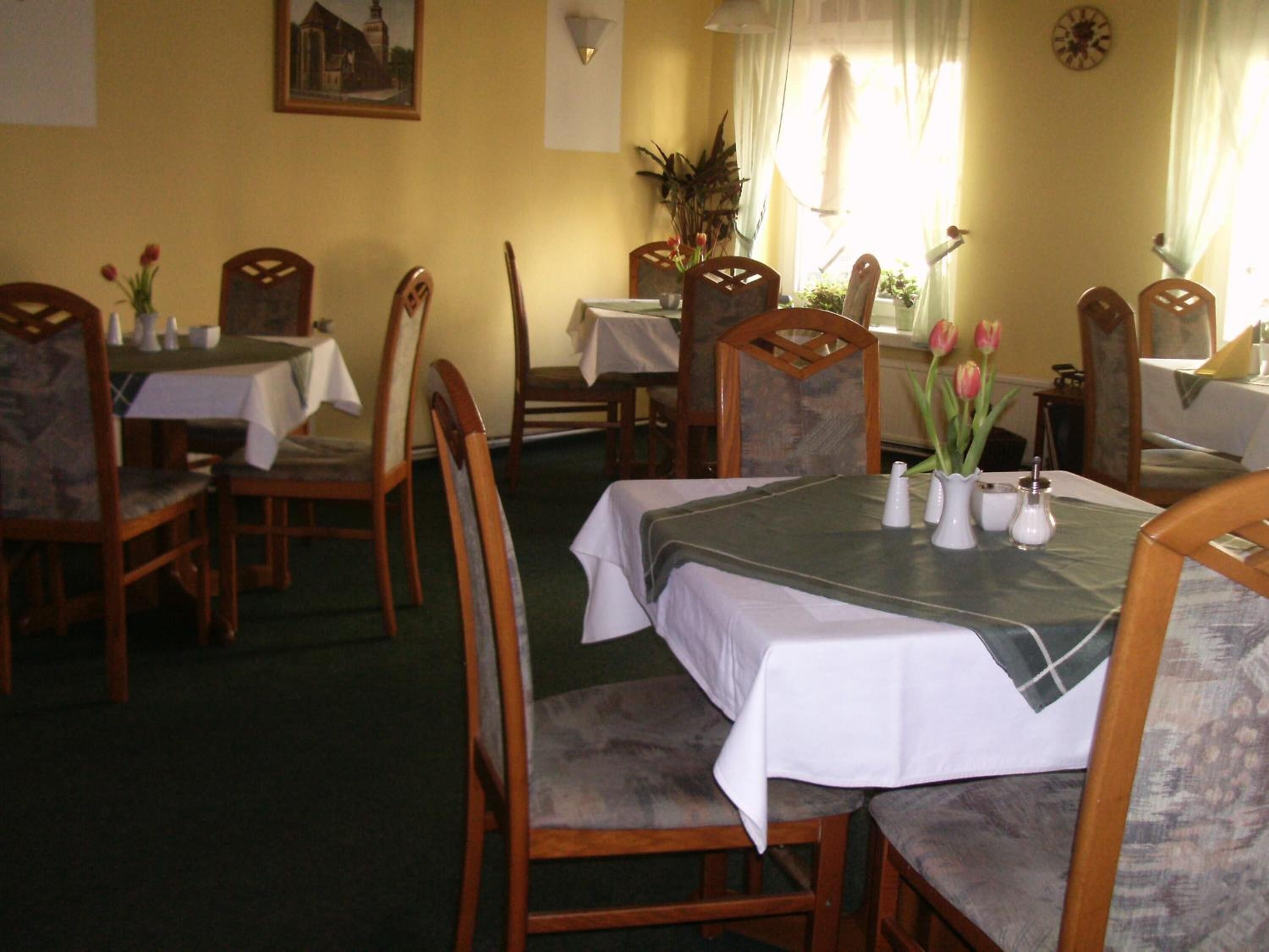 Un espace repas avec des tables et des chaises, un tableau accroché au mur et une fenêtre avec des rideaux.