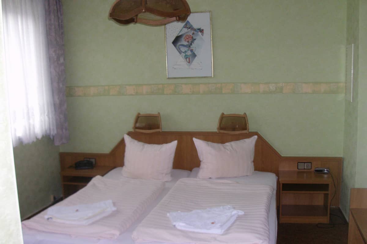 A double bed with two pillows, a bedside table, a nightstand, and a wall-mounted lamp.