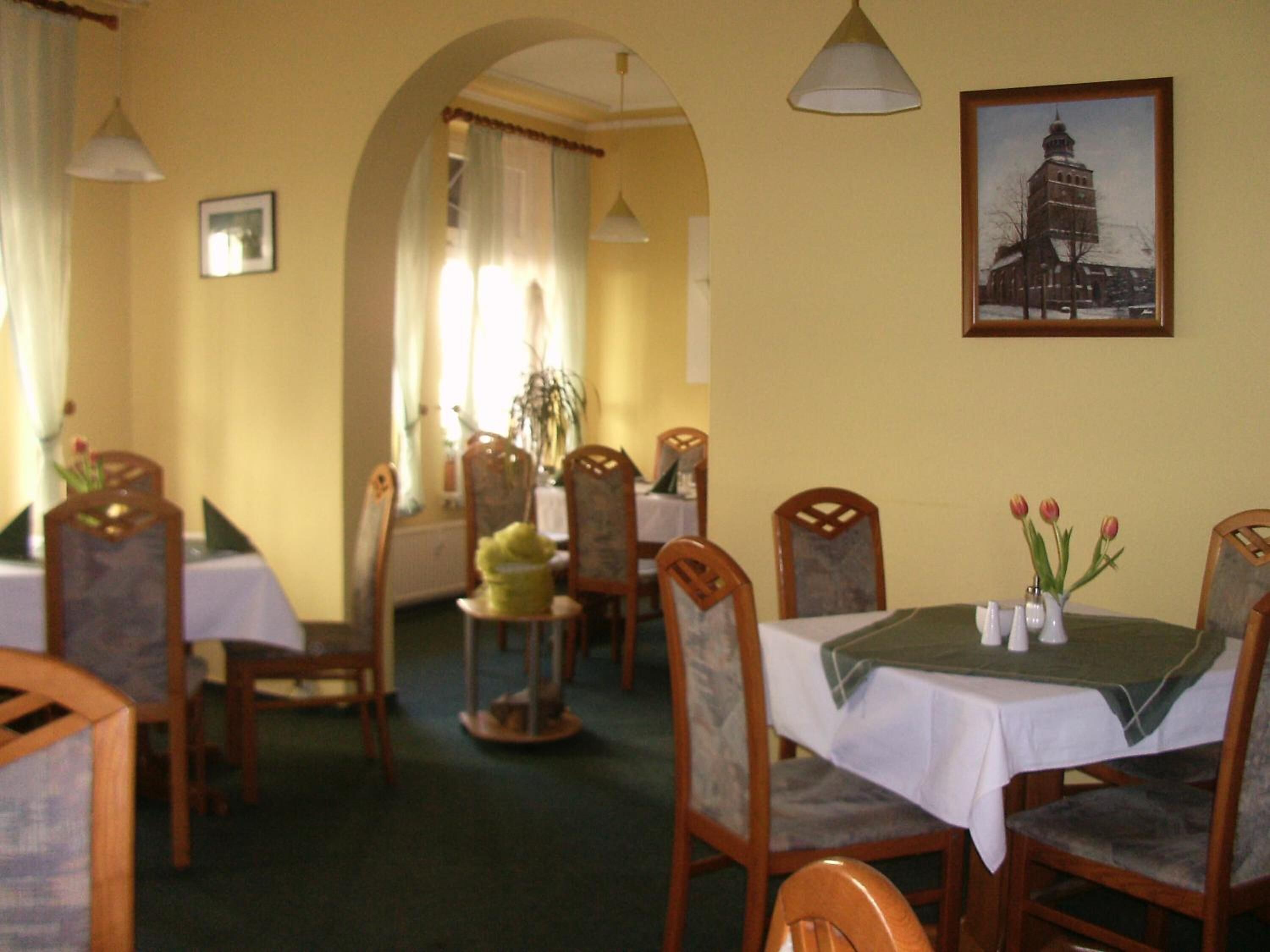 A dining area with wooden chairs and tables, a chandelier, and a framed picture on the wall.