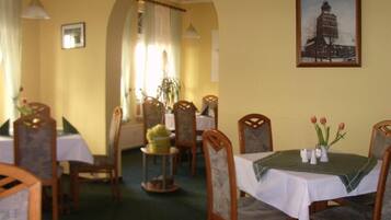 A dining area with wooden chairs and tables, a chandelier, and a framed picture on the wall.
