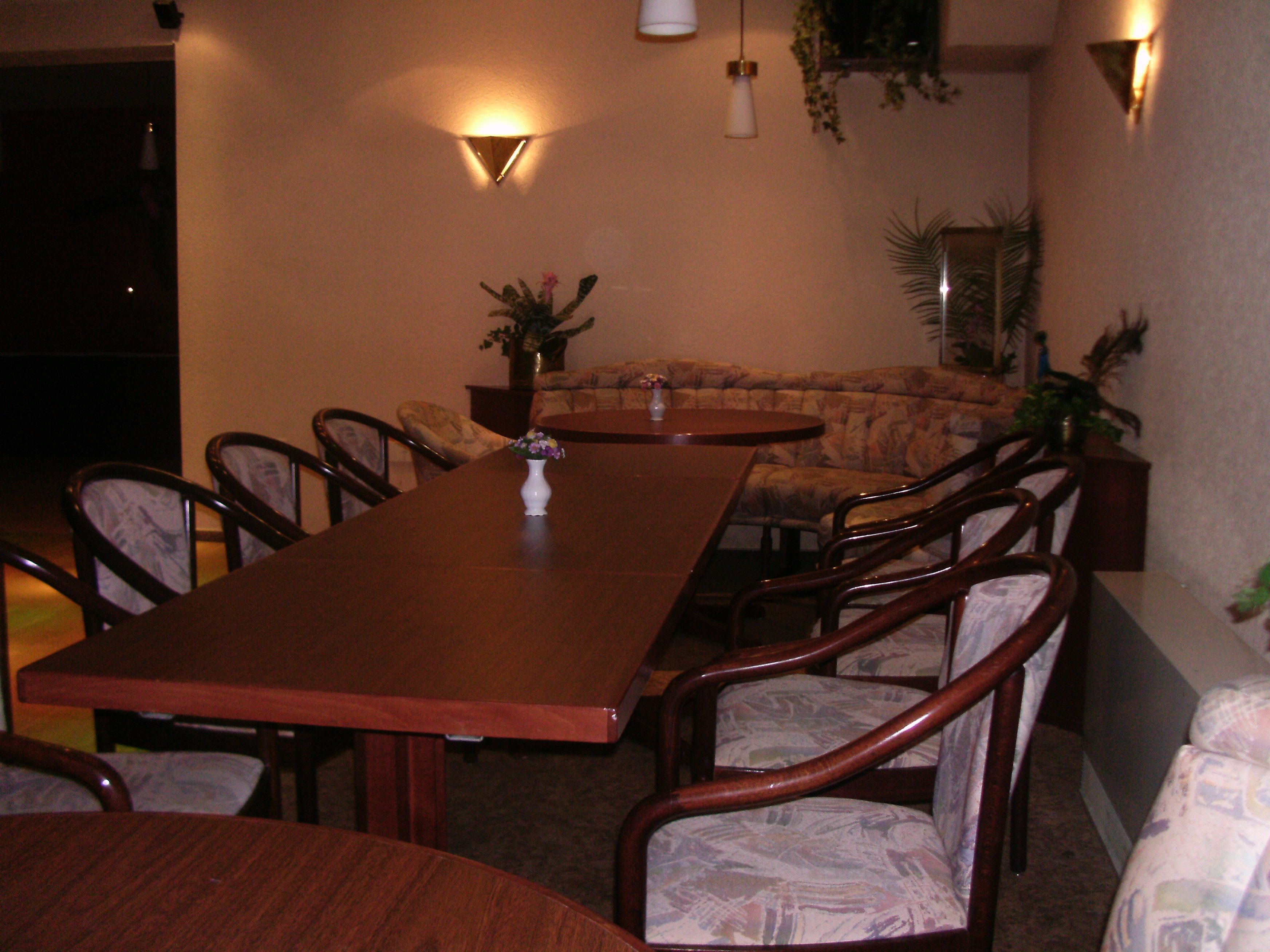 Un comedor con una mesa de madera alargada, varias sillas, un sofá e iluminación instalada en la pared.