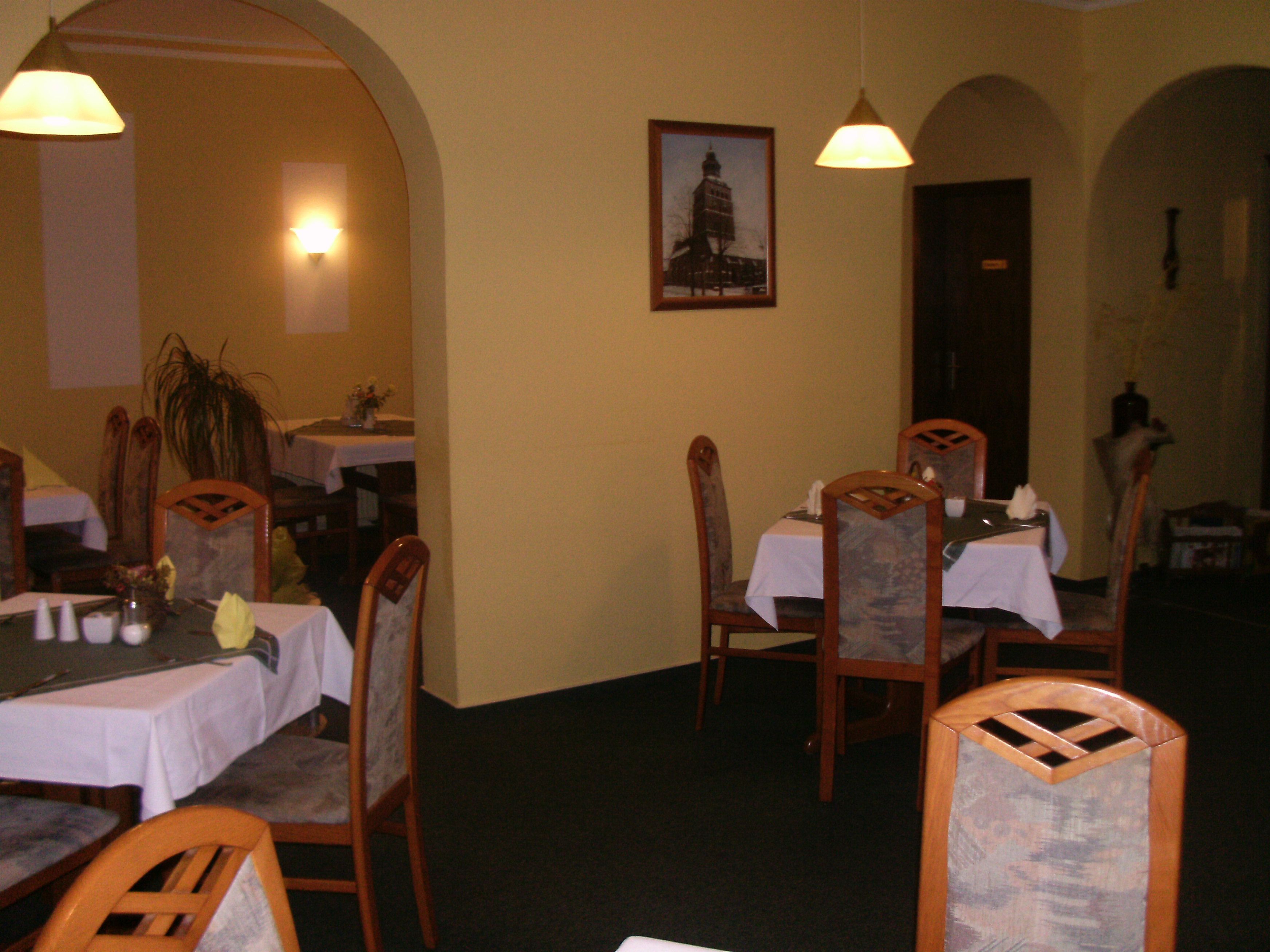 Un comedor con mesas dispuestas para cuatro personas, sillas de madera y lámparas colgantes.