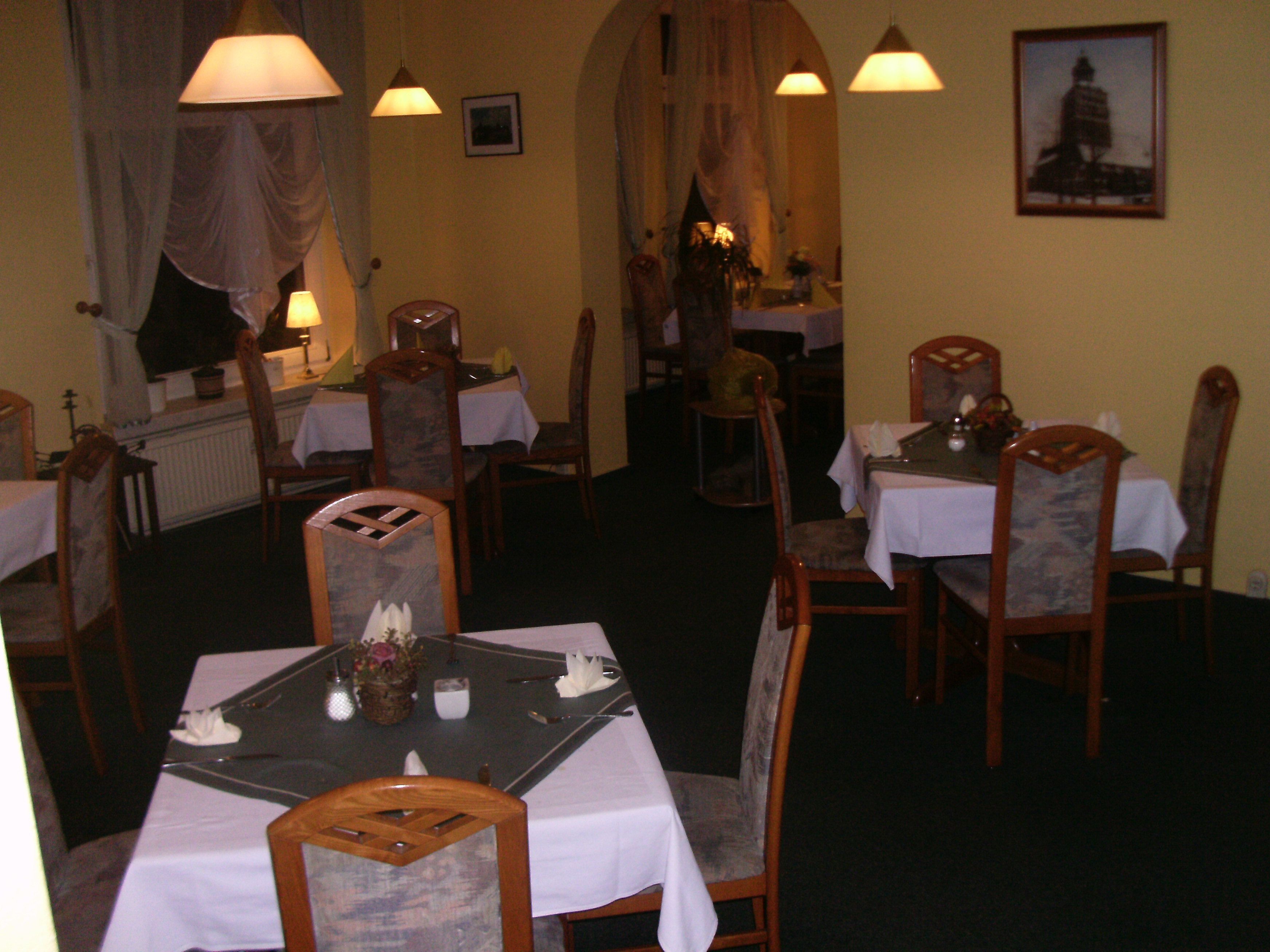 Un comedor con mesas dispuestas para dos, sillas de madera y lámparas colgantes.
