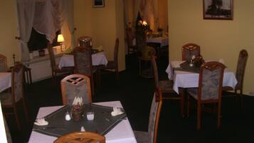 Un comedor con mesas dispuestas para dos, sillas de madera y lámparas colgantes.