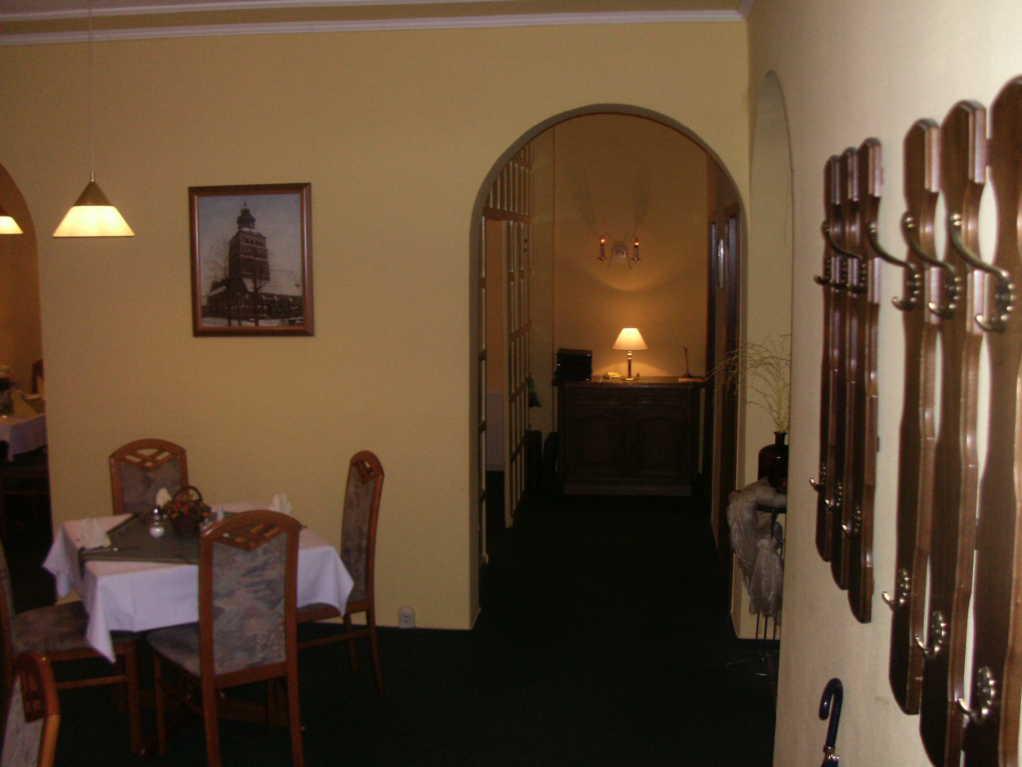 Ein Essbereich mit einem für zwei Personen gedecktem Tisch, Stühlen, einem gerahmten Bild an der Wand und einem Gang, der in einen anderen Raum führt.