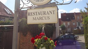 A sign for 'Warsteiner' beer and 'RESTAURANT MARCUS' with a hanging flower pot. - Hotel-Restaurant Marcus (Malchin)