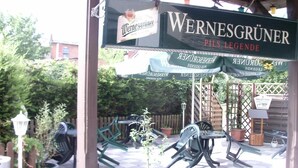 An outdoor seating area with tables and chairs, a sign for 'Wernesgruner Pils Legende', and a sign indicating a toilet. - Hotel-Restaurant Marcus (Malchin)
