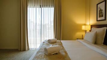 Una habitación de hotel con una cama grande, una mesita de noche con lámpara y una ventana con cortinas.