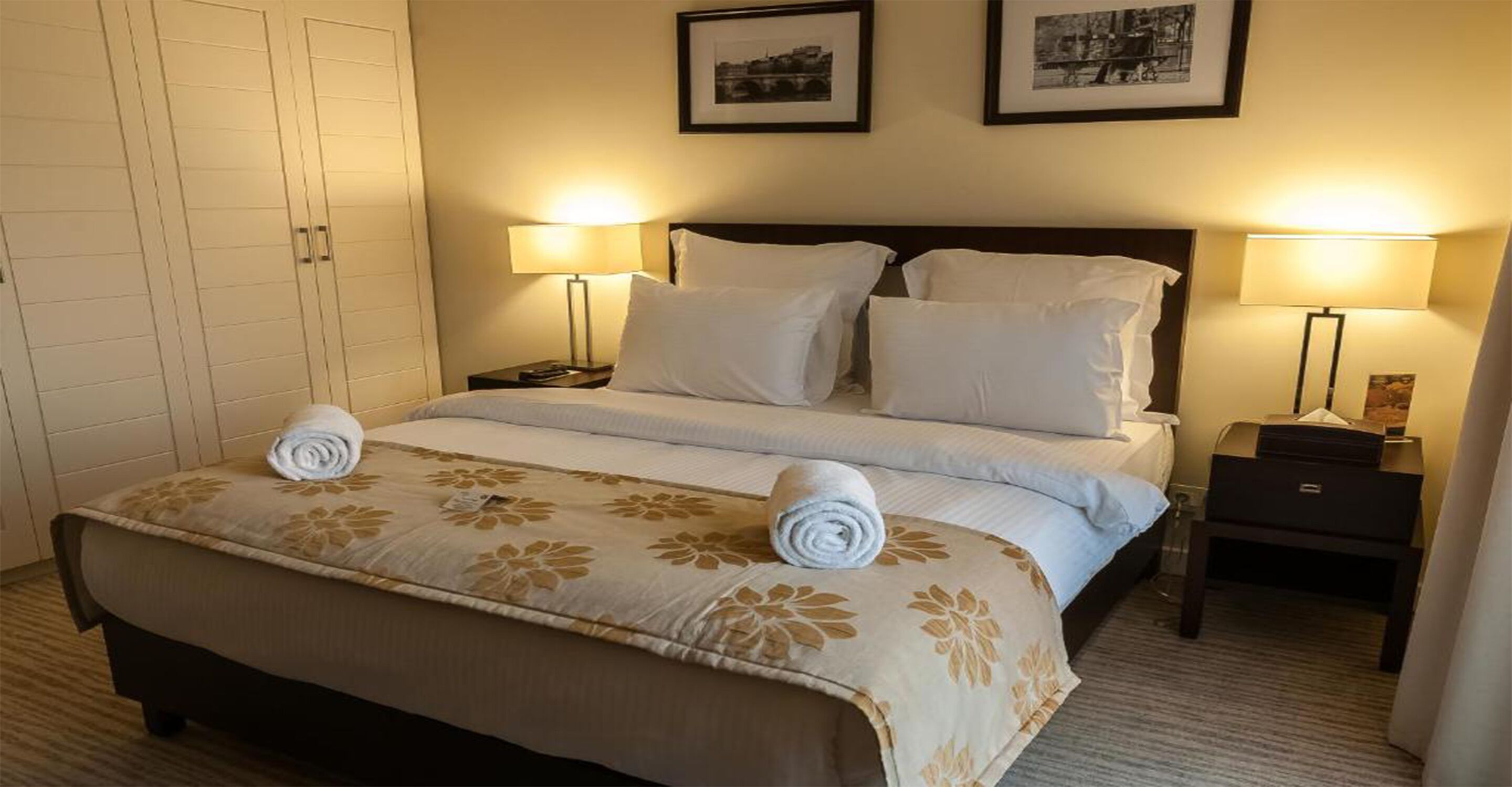 Una habitación de hotel con una cama grande, dos lámparas de noche, una mesita de noche y un armario.