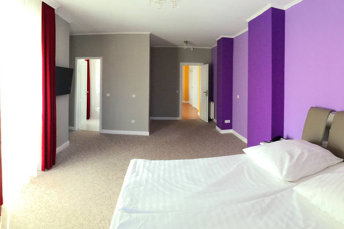 A hotel room with a bed, a television, and a hallway leading to another room.