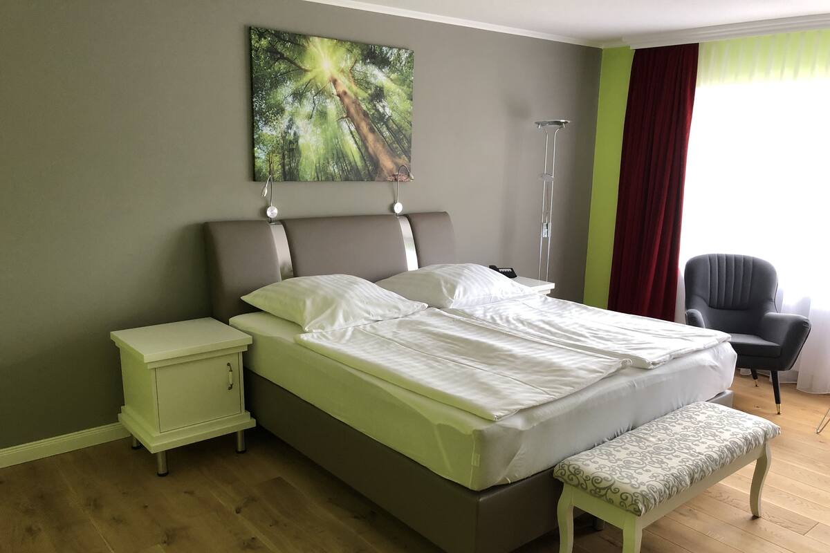 A bedroom with a bed, bedside tables, a bench, a chair, and a painting on the wall.