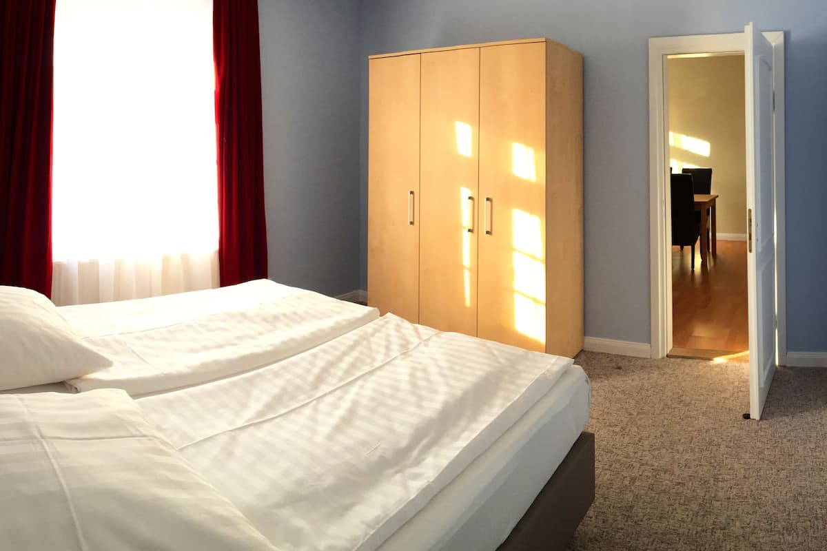 A neatly made bed with white linens and a headboard, a wardrobe with sliding doors, and a doorway leading to another room.