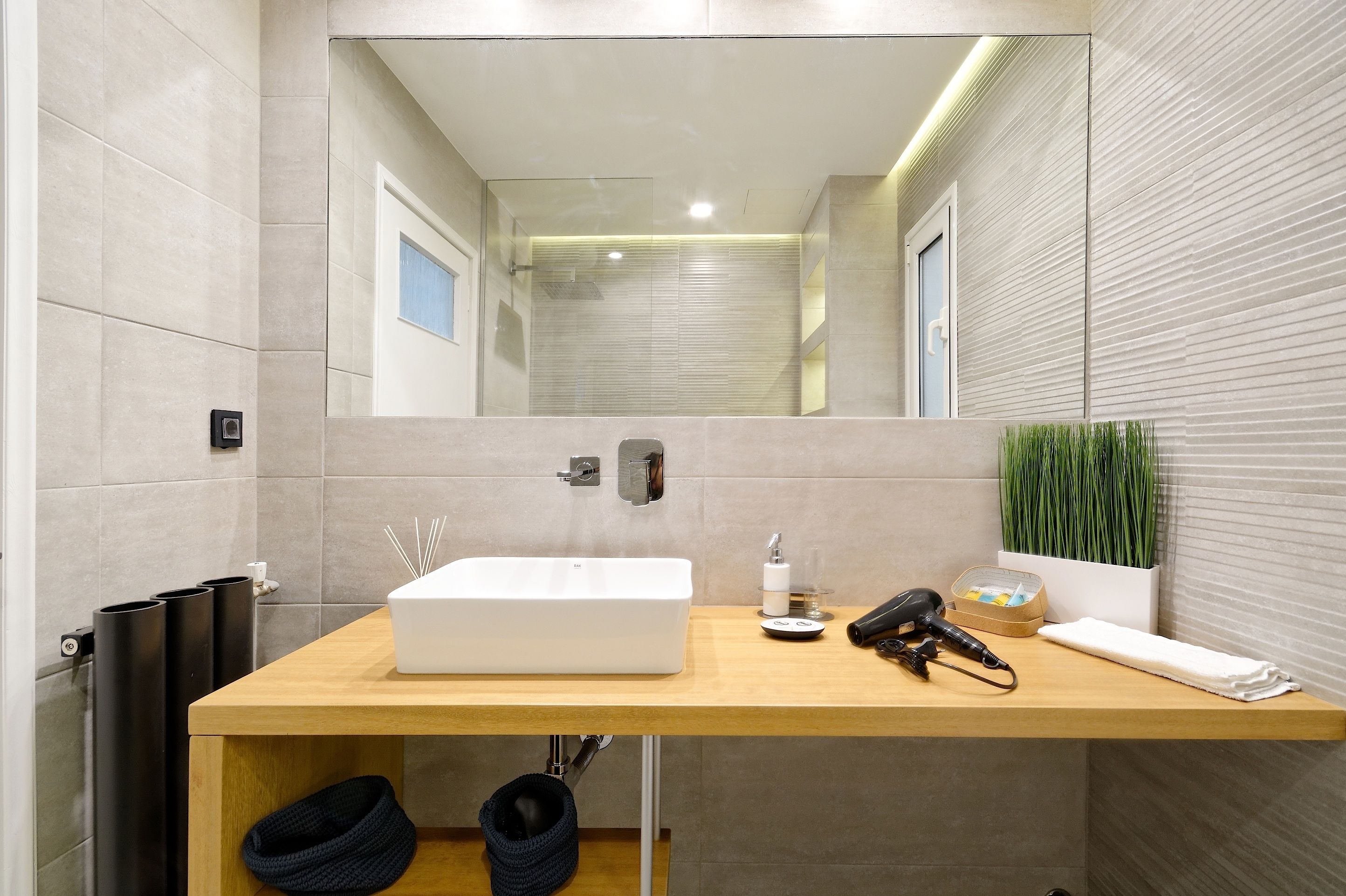 Un baño moderno con un espejo grande, un lavabo blanco, una toalla y un secador de pelo en la encimera.