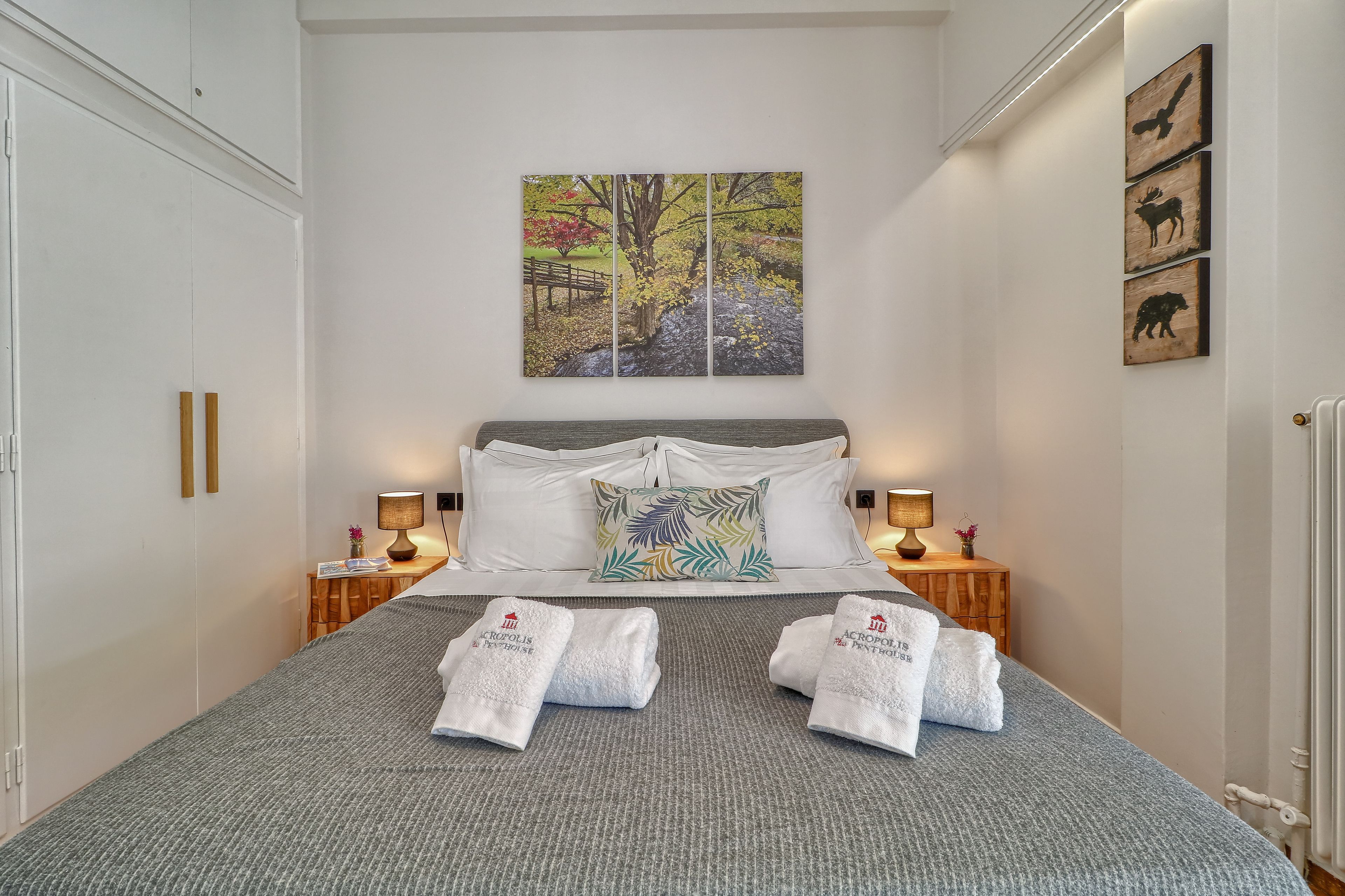 A neatly made bed with towels, a painting of a tree, and a wooden cabinet.