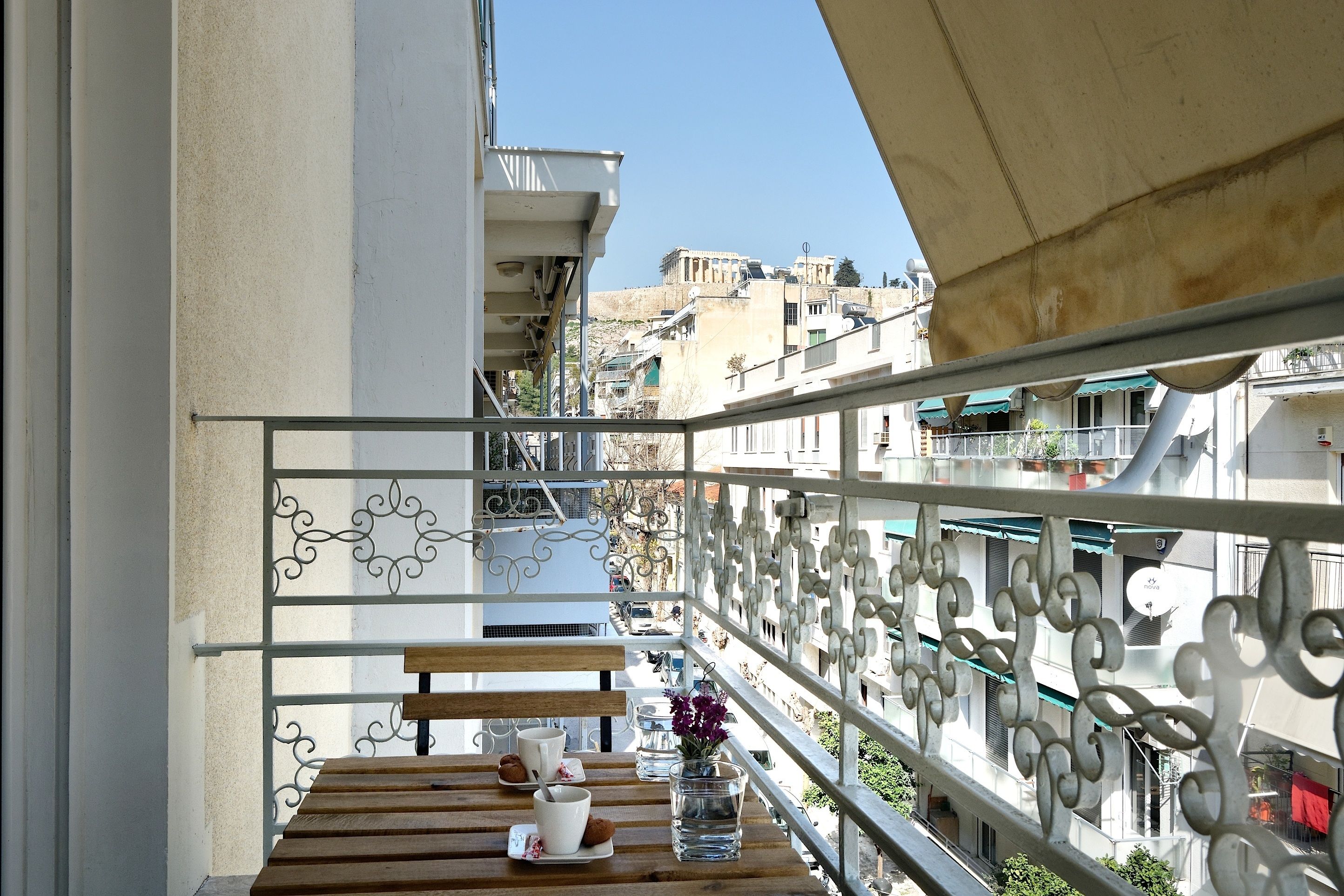 Un balcon avec une table en bois, une rambarde en métal et une vue sur les bâtiments en arrière-plan.