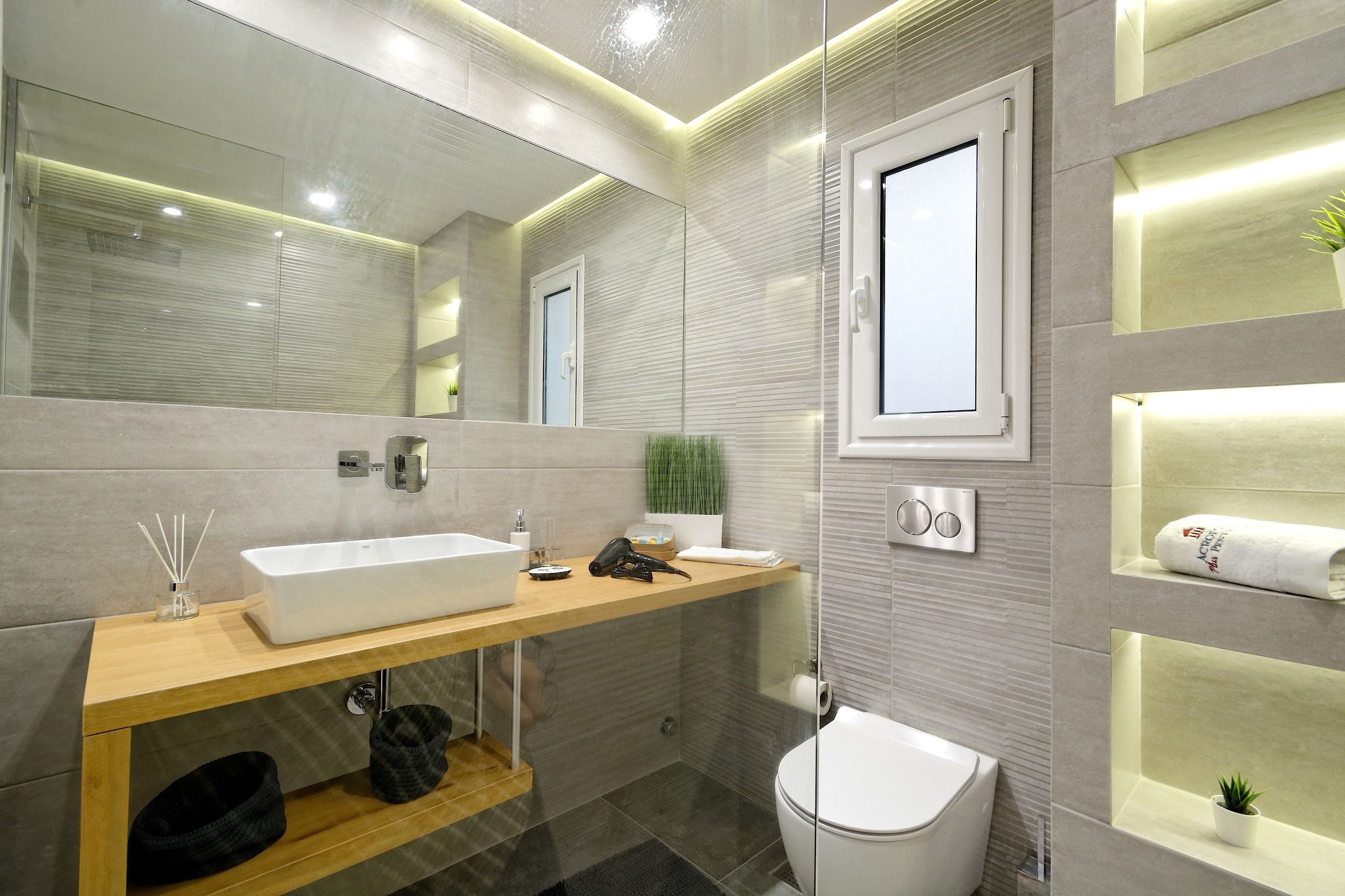 Une salle de bain moderne avec un grand miroir, un lavabo blanc, des toilettes et un espace douche.