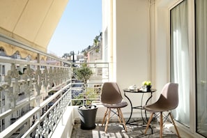 Un balcon agrémenté d’un pot de fleurs, de deux chaises, d’une petite table et offrant une vue sur le paysage urbain.