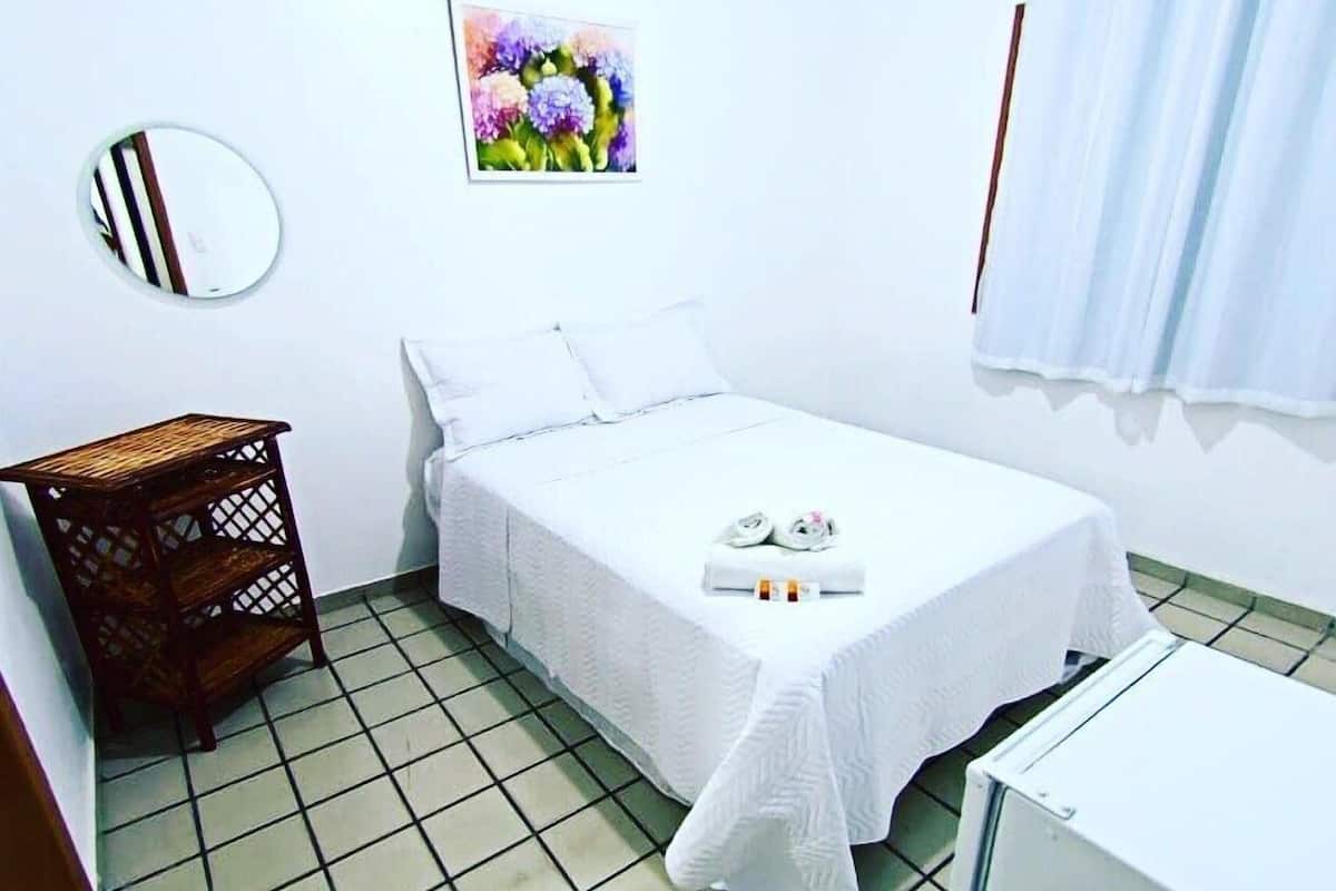 Une petite pièce propre, avec un lit, une petite table, un miroir et un tableau accroché au mur.