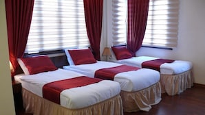 Habitación de hotel con tres camas individuales, cada una con una manta roja y ropa de cama blanca. La habitación tiene suelo de madera y ventanas amplias con cortinas rojas.