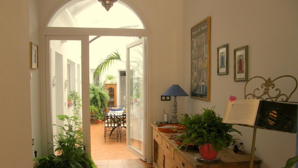 A hallway with a tiled floor, a wooden cabinet with a potted plant, a framed picture, and a lamp.