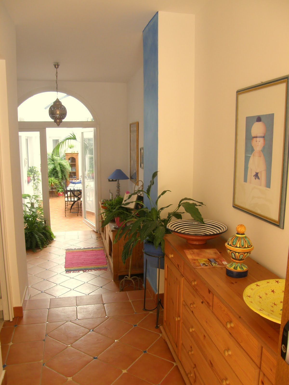 Um corredor com chão de azulejos, um armário de madeira, uma parede azul e uma porta que dá para um pátio.