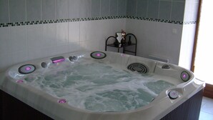 A large, rectangular hot tub with multiple jets, set against a tiled wall with a decorative border. - Chez Louis - Chambres d'Hôtes (La Canourgue)