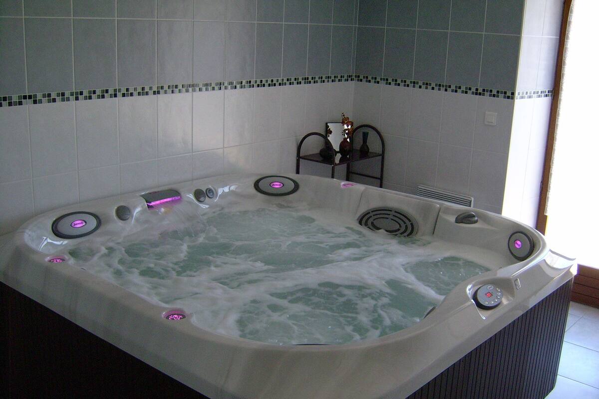 A large, rectangular hot tub with multiple jets, set against a tiled wall with a decorative border.