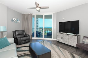 Una sala de estar moderna con una televisión de pantalla plana, un sillón de cuero y vistas a un edificio a través de puertas de vidrio grandes.