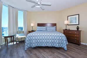 A bedroom with a large bed, a chair, a dresser, a lamp, and a ceiling fan. - Spacious open-concept resort condo w/private balcony in Destin! (Destin)