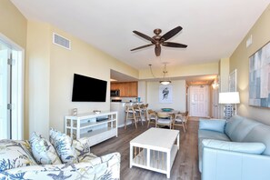 Ein Wohnzimmer mit Sofa, Fernseher, Deckenventilator, Essbereich und Küche.
