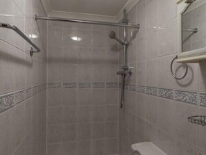A shower area with a glass door, a handheld showerhead, and a towel rack.