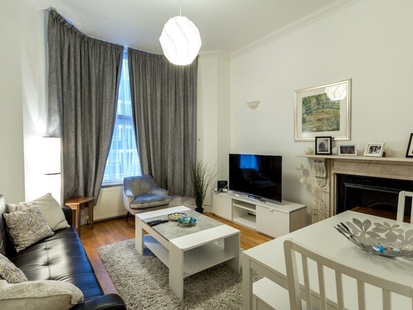 A modern living room with a sofa, coffee table, TV, fireplace, and large window with curtains.