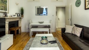 A living room with a fireplace, a dining table, a sofa, and a coffee table with decorative items. - Spacious Centrally Located One Bed (London)