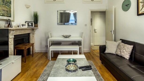 A living room with a fireplace, a dining table, a sofa, and a coffee table with decorative items. - Spacious Centrally Located One Bed (London)