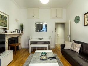 A living room with a fireplace, a dining table, a sofa, and a coffee table with decorative items. - Spacious Centrally Located One Bed (London)