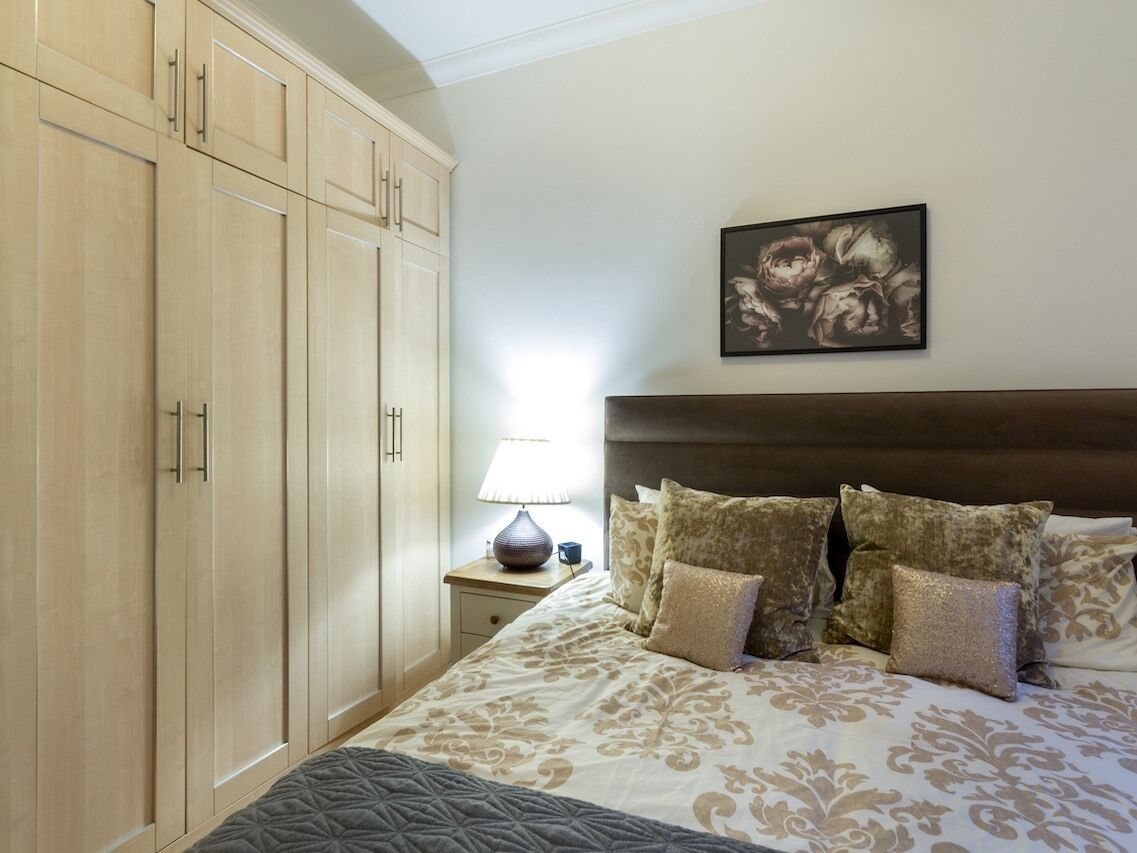 A bedroom with a bed, a nightstand, a lamp, a framed picture on the wall, and wooden cabinets.