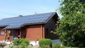 Une maison dotée de panneaux solaires sur le toit et d’un jardin bien entretenu.