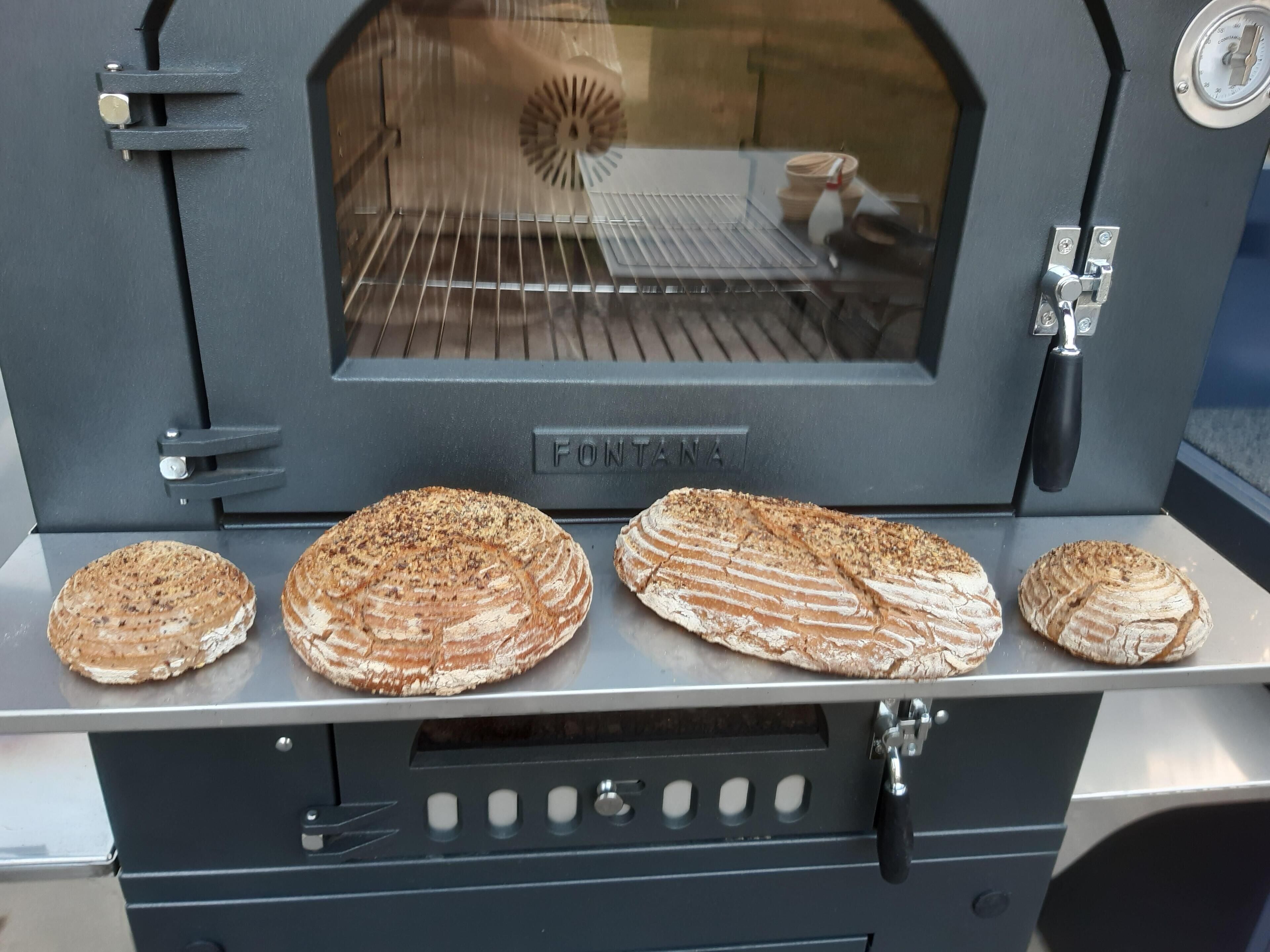 A stone oven with four loaves of bread on the top shelf.