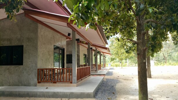 A building with a concrete facade, multiple windows, and a covered porch area with wooden railings. - Baan Keree Thara Khiri Wong (Lan Saka)