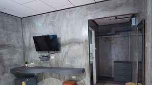 A modern bathroom with a marble wall, a built-in TV, a vanity with a mirror, and a walk-in closet. - Baan Keree Thara Khiri Wong (Lan Saka)