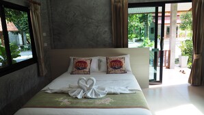 A hotel room with a bed, two pillows with 'LOVE' text, a green floral bedspread, and a view of greenery outside. - Baan Keree Thara Khiri Wong (Lan Saka)