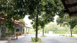 A covered outdoor area with a building featuring a red roof and a gravel path. - Baan Keree Thara Khiri Wong (Lan Saka)