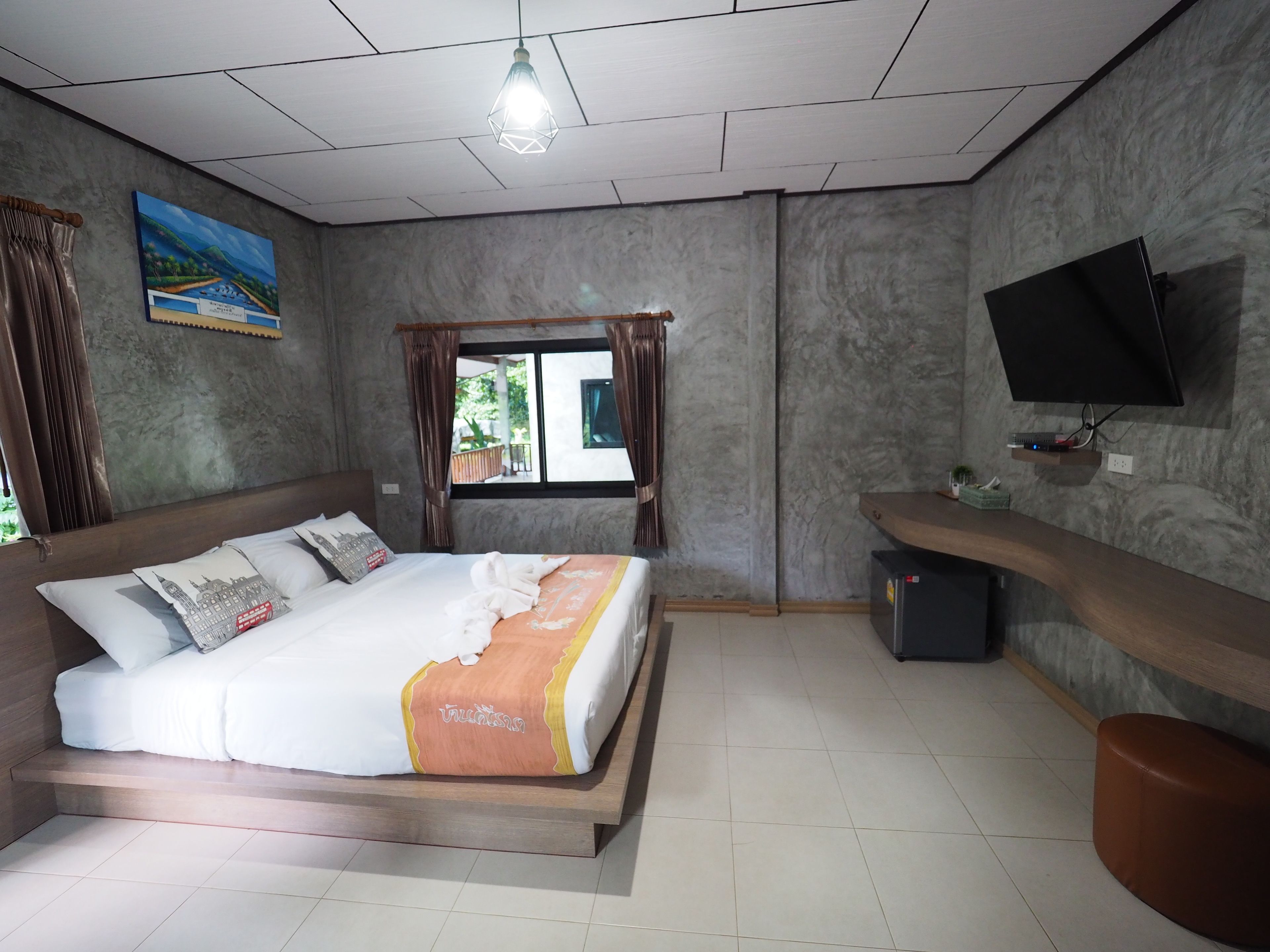A hotel room with a bed, a TV mounted on the wall, a window with curtains, and a painting on the wall.