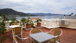 Una terraza en la azotea con mobiliario exterior, plantas en macetas y vistas al mar y a las montañas.