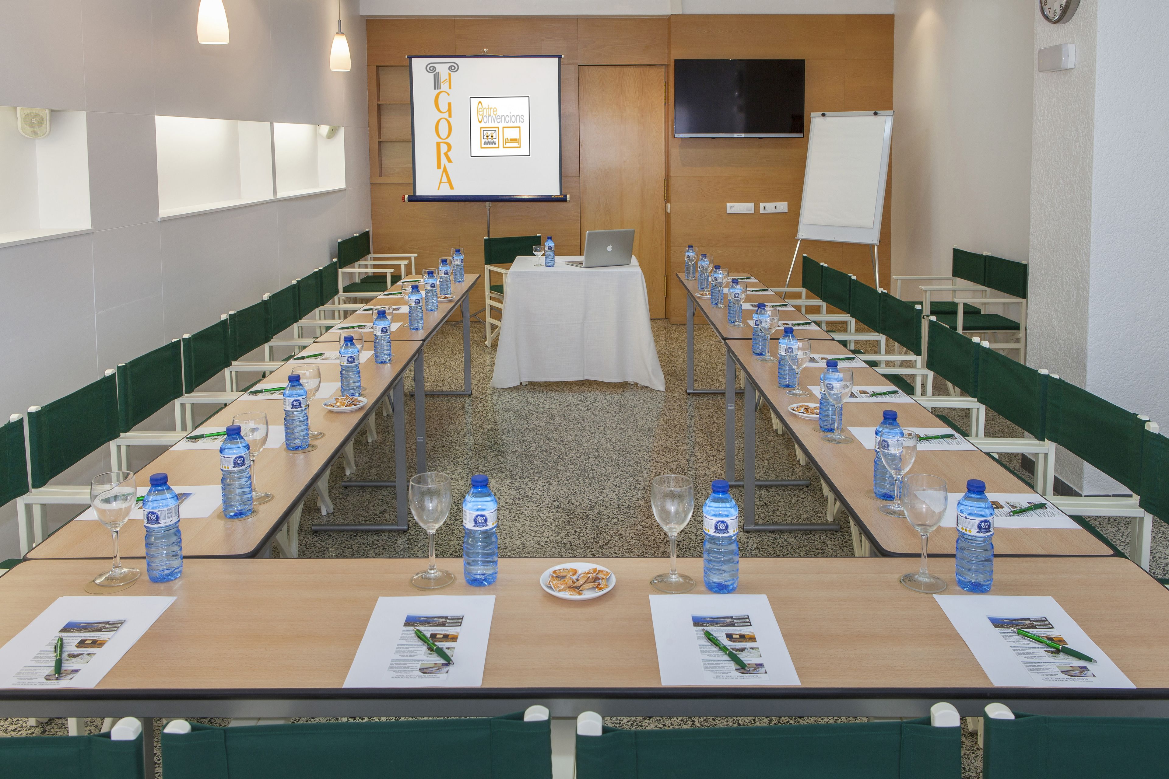 Un salón de conferencias con largas mesas, botellas de agua y vasos.